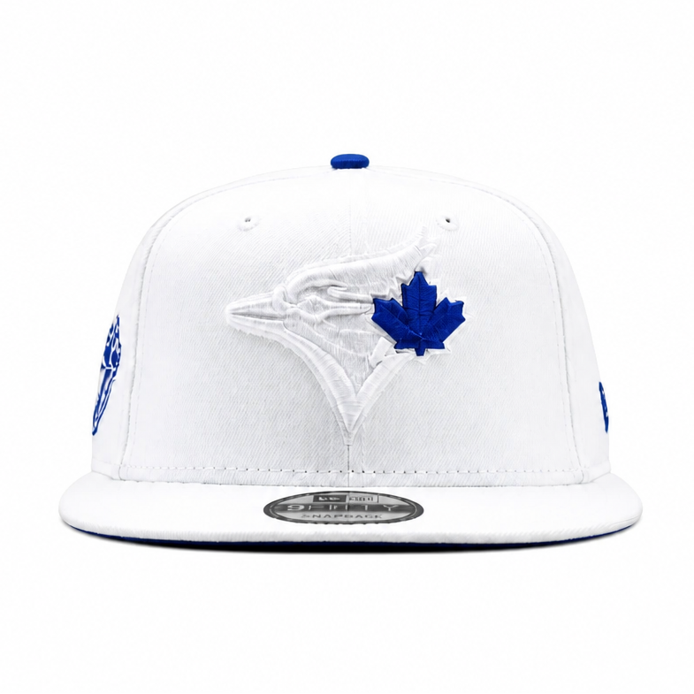 A white Toronto Blue Jays snapback cap featuring a white and blue embroidered bird logo with a blue maple leaf on the front, set against a plain white background.