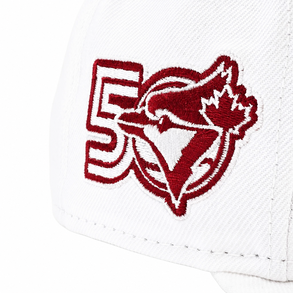 Close-up of a white baseball cap featuring an embroidered red and white Toronto Blue Jays 50th anniversary logo on the side.