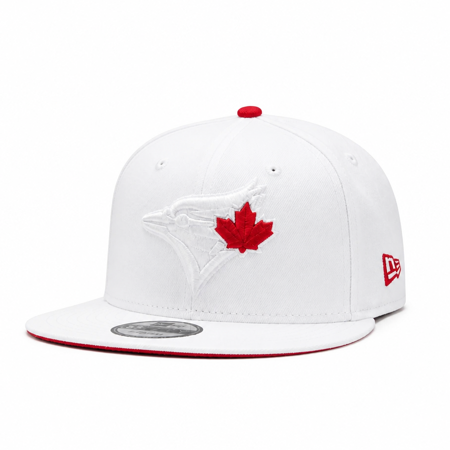 A white flat-brim baseball cap featuring an embroidered white Toronto Blue Jays bird logo and a red maple leaf on the front, with a red button on top, a red brim edge, and a red New Era logo on the side.